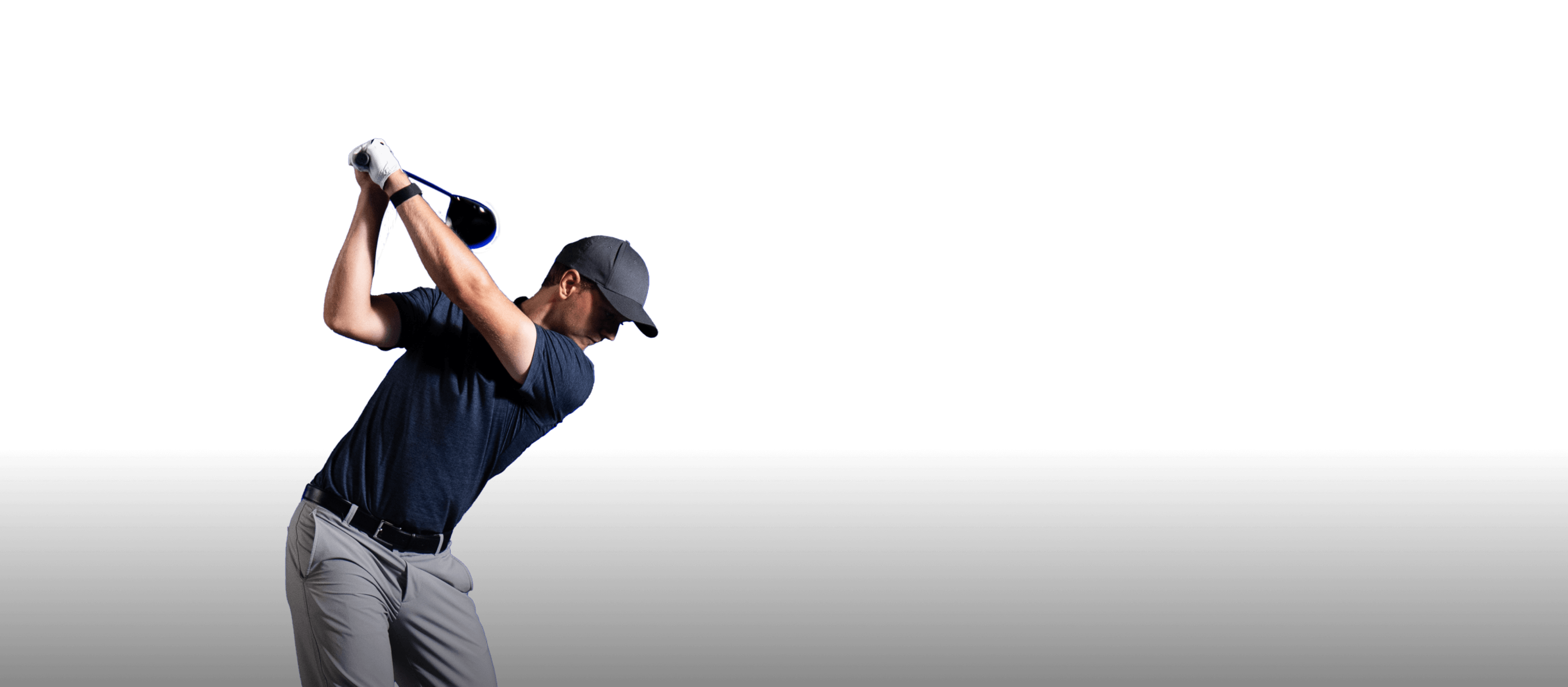 Golfer in a navy shirt and gray pants swings a club against a black background.